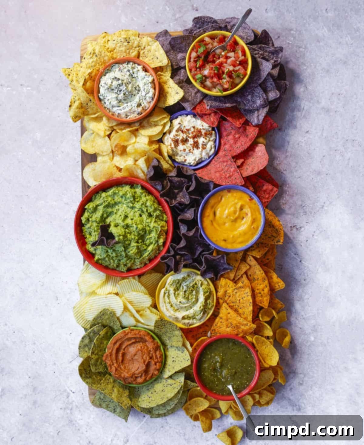 A beautifully arranged chips and dips board by The BakerMama, featuring an assortment of colorful dips and various crispy chips, perfect for entertaining.