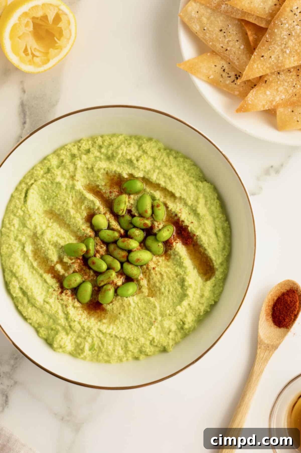 Smooth and creamy edamame hummus in a white bowl, garnished with a sprinkle of red pepper flakes.
