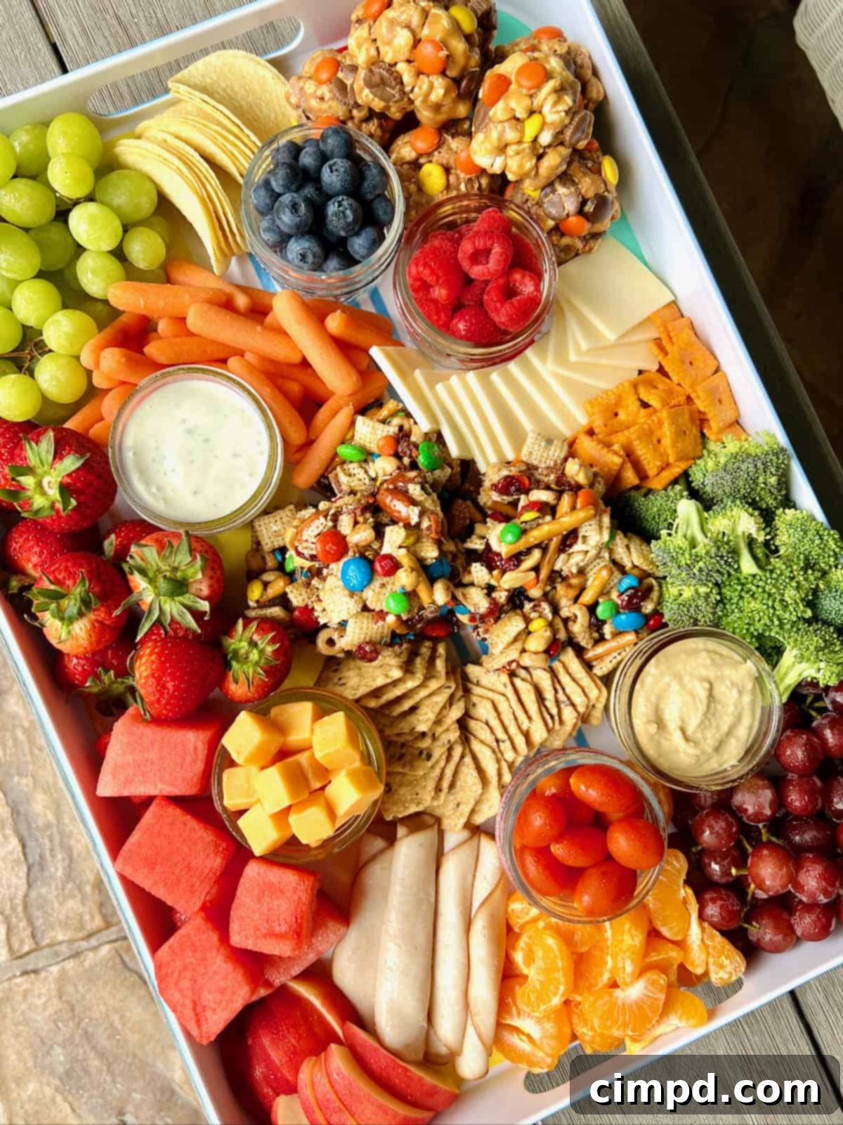 Picnic Perfection Platter 2 A beautifully arranged white snack tray brimming with fresh fruits, assorted cheeses, delightful popcorn balls, and wholesome snack bars, perfect for a summer picnic.