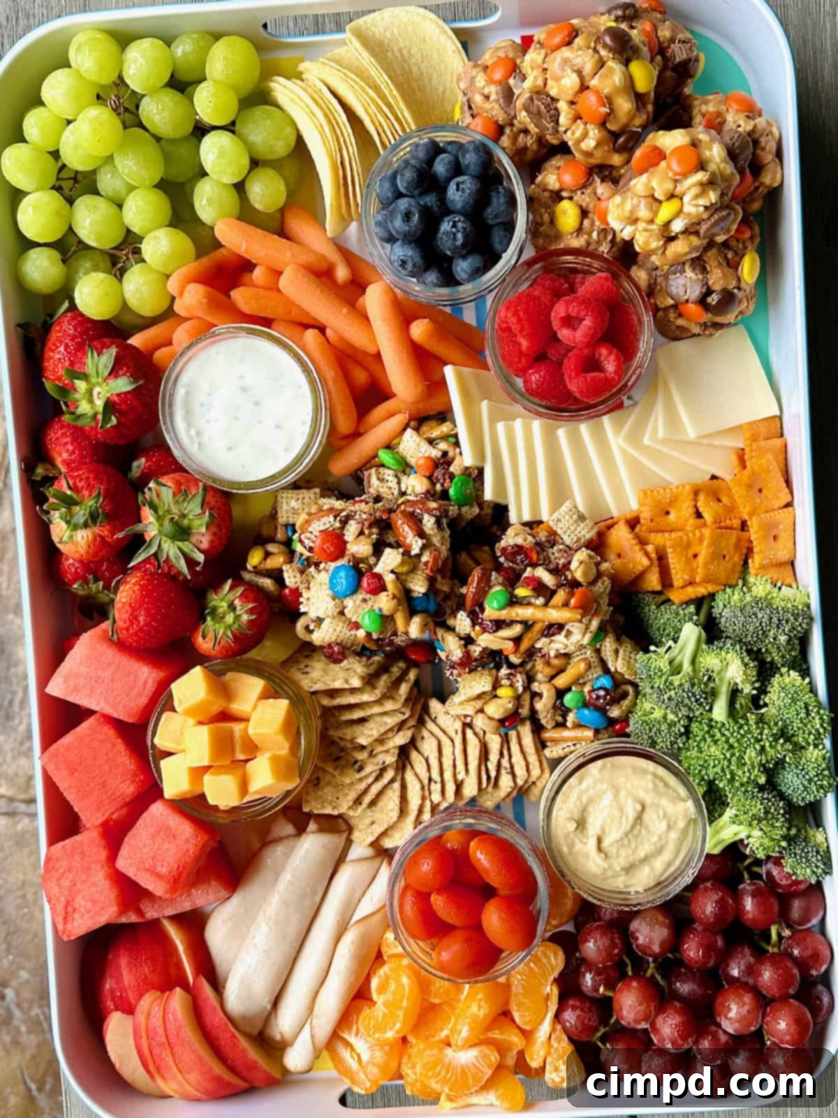 Picnic Perfection Platter 4 A pristine white snack tray, generously laden with a vibrant assortment of fresh fruits, an array of delectable cheeses, whimsical popcorn balls, and satisfying snack bars, poised for a delightful outdoor gathering.