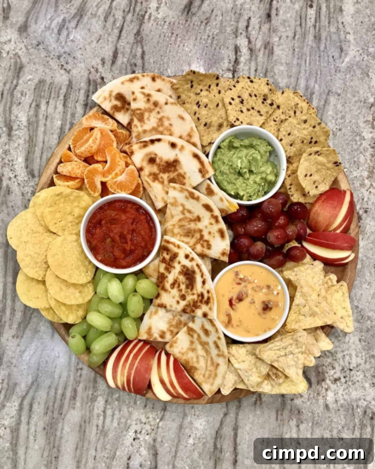 A colorful Quesadilla Lunch Board by The BakerMama, featuring quesadilla wedges, chips, various dips, and fresh fruit arranged for a delightful meal.