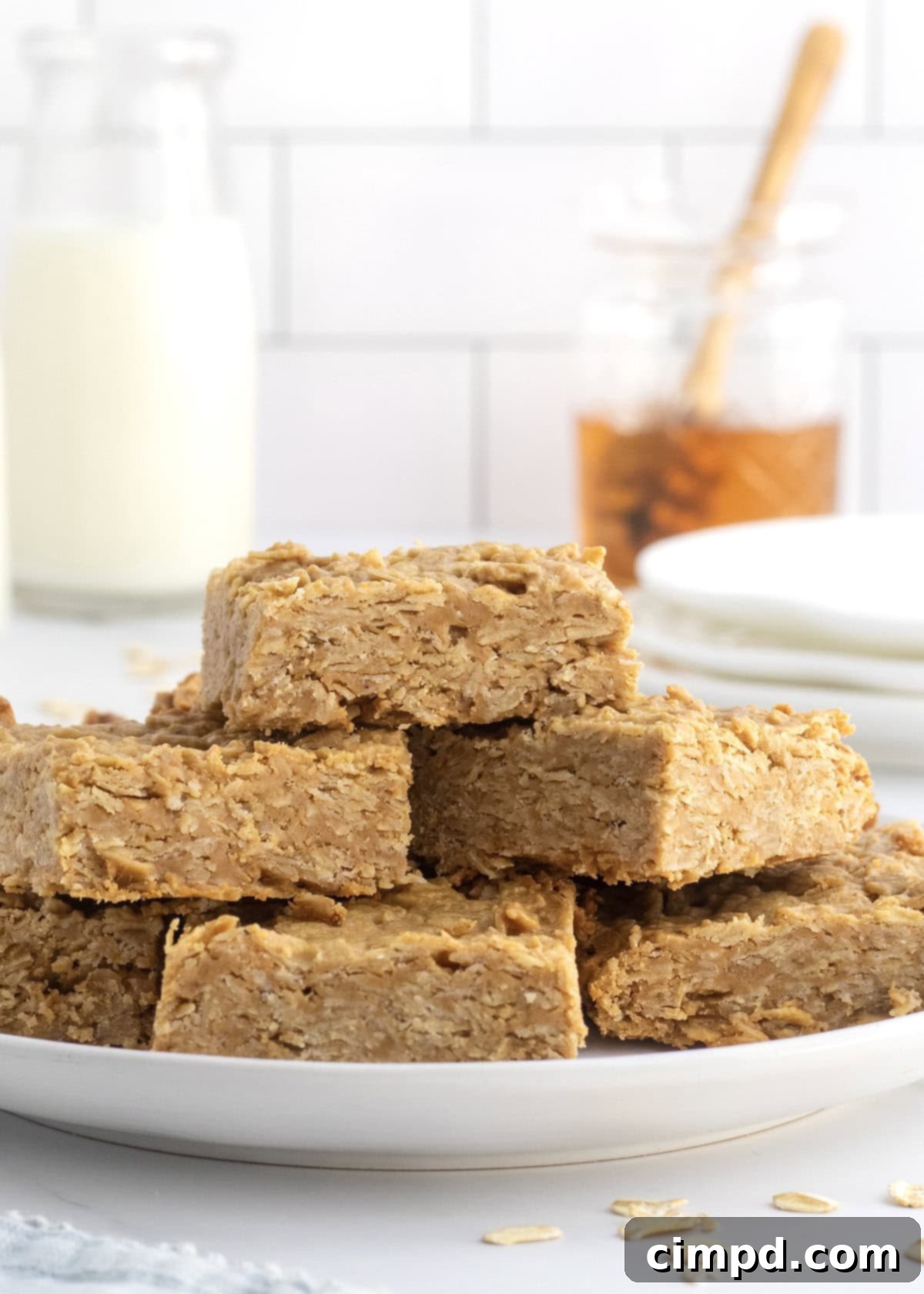 Six golden-brown peanut butter honey oat bars stacked on a white plate, showcasing their perfect texture.