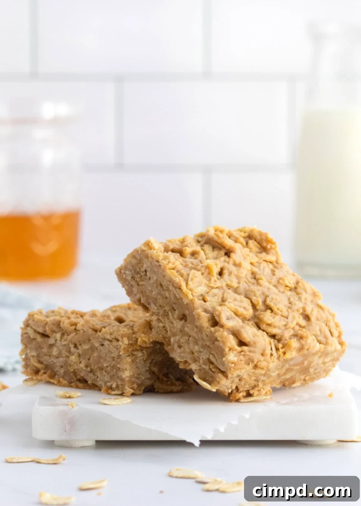 Two golden peanut butter honey oat bars resting on a white marble surface next to a jar of honey, inviting a sweet treat.