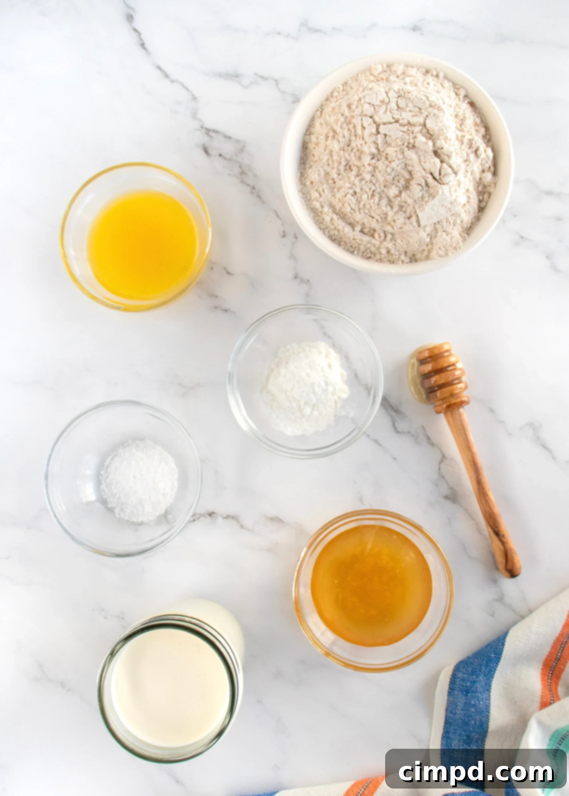 Wholesome Honey Wheat Biscuits 6 Key ingredients for Honey Whole Wheat Biscuits laid out on a wooden surface: whole wheat flour, baking powder, salt, heavy cream, honey, and melted butter.
