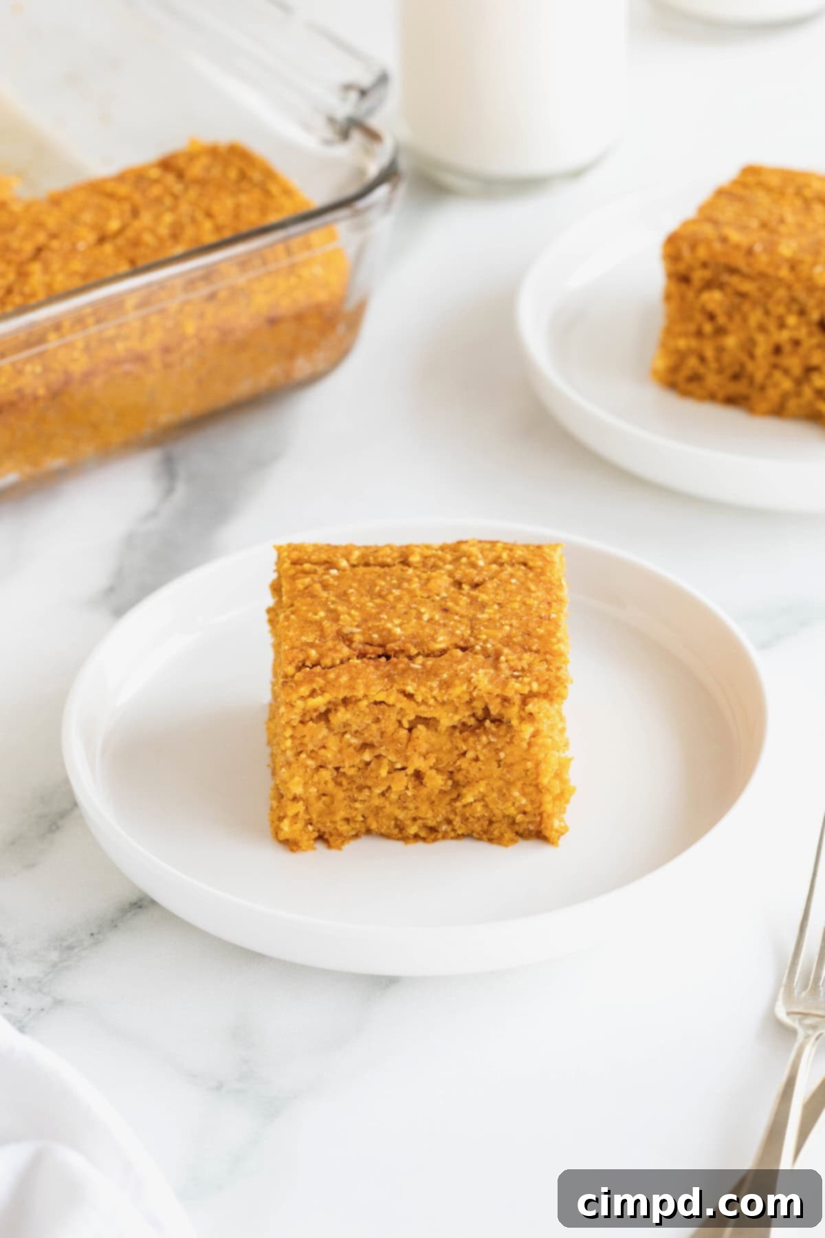 A single square piece of golden-brown pumpkin cornbread, with a small bite taken out, artfully placed on a small white-rimmed plate.