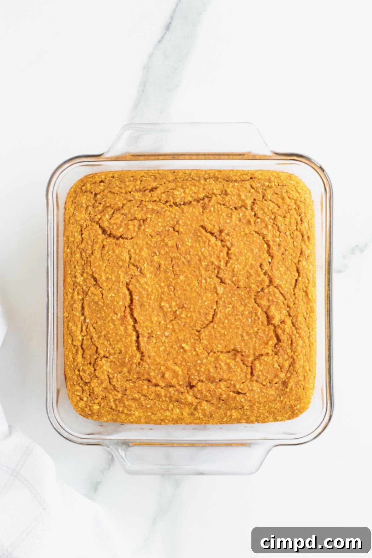 A perfectly baked, golden-brown whole wheat pumpkin cornbread resting invitingly in its square glass baking dish.
