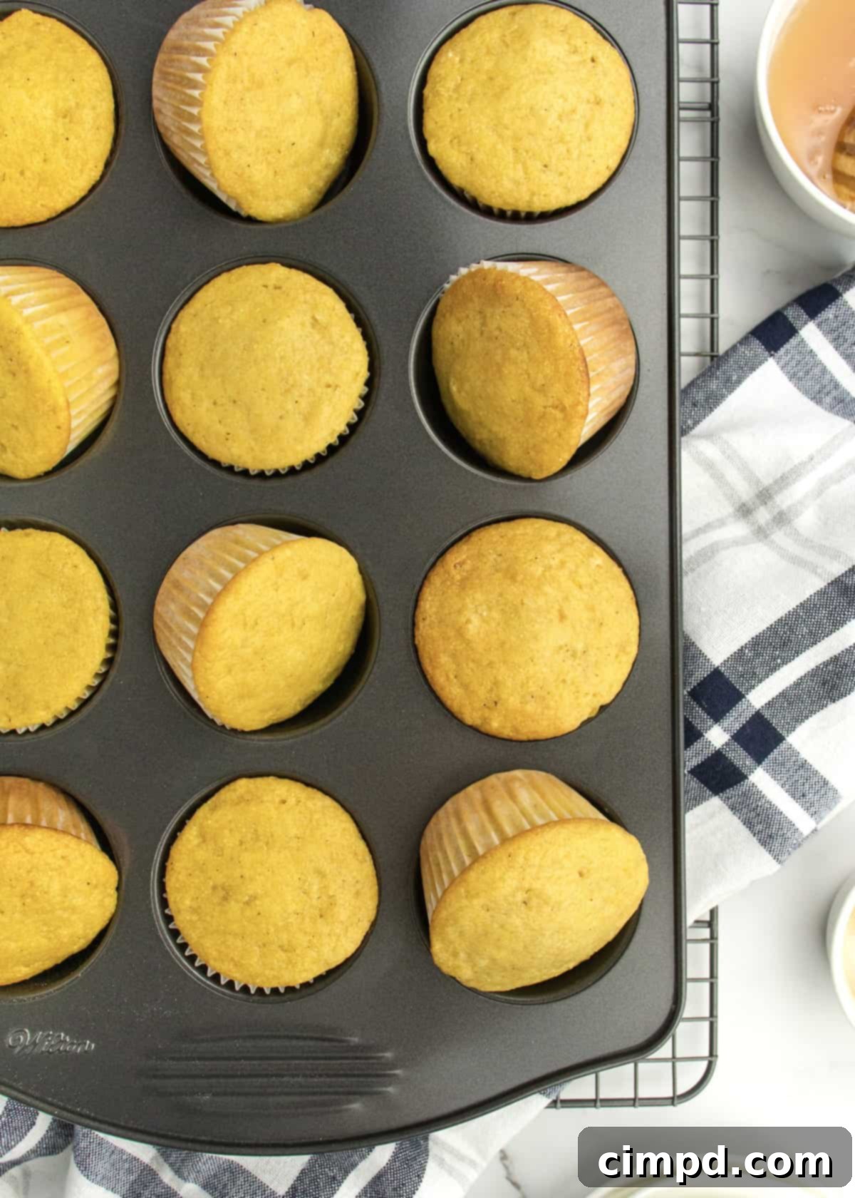 Honey corn muffins cooling in a 12-cup dark muffin tin.
