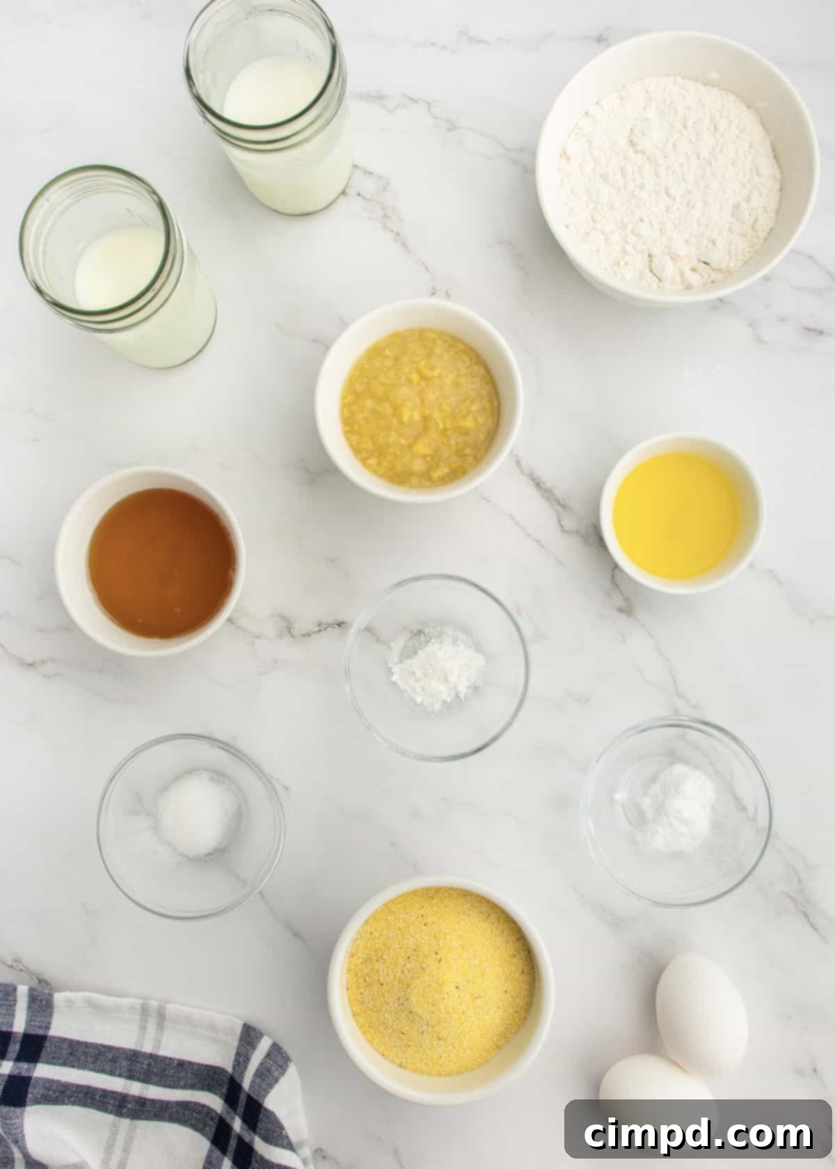 Ingredients for honey corn muffins laid out in small glass dishes on a white marble counter.