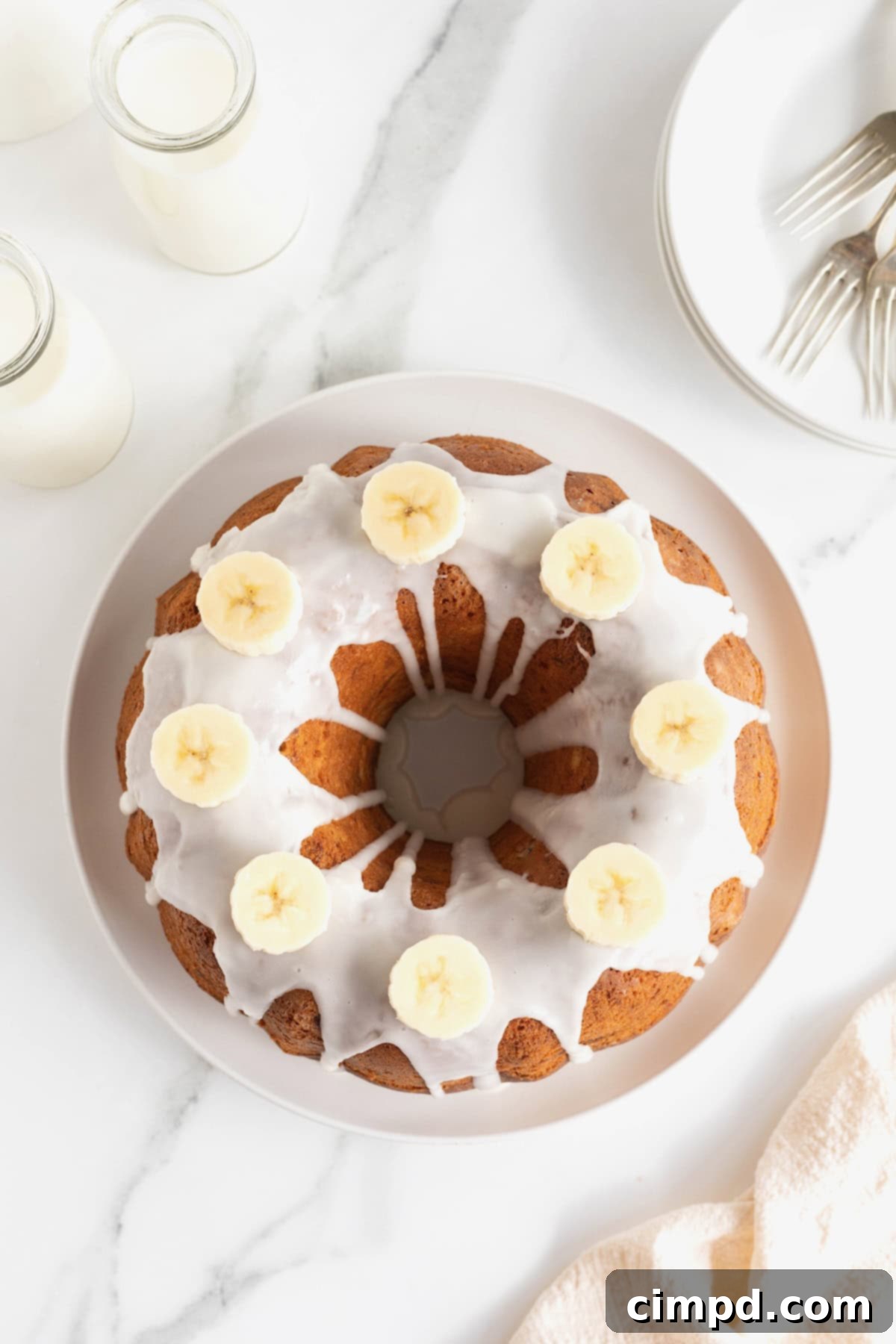Seen from above, a glazed pound cake garnished with banana slices on a white serving plate.