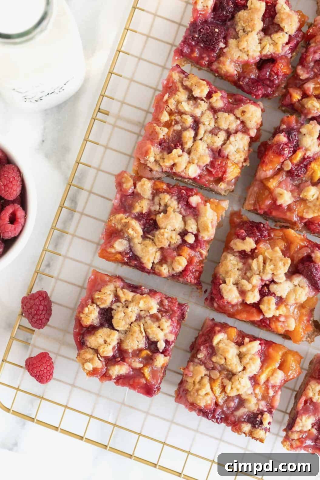 Rustic Peach Raspberry Crumbles 11 Peach raspberry crumb bars on a parchment lined gold-toned wire cooling rack.