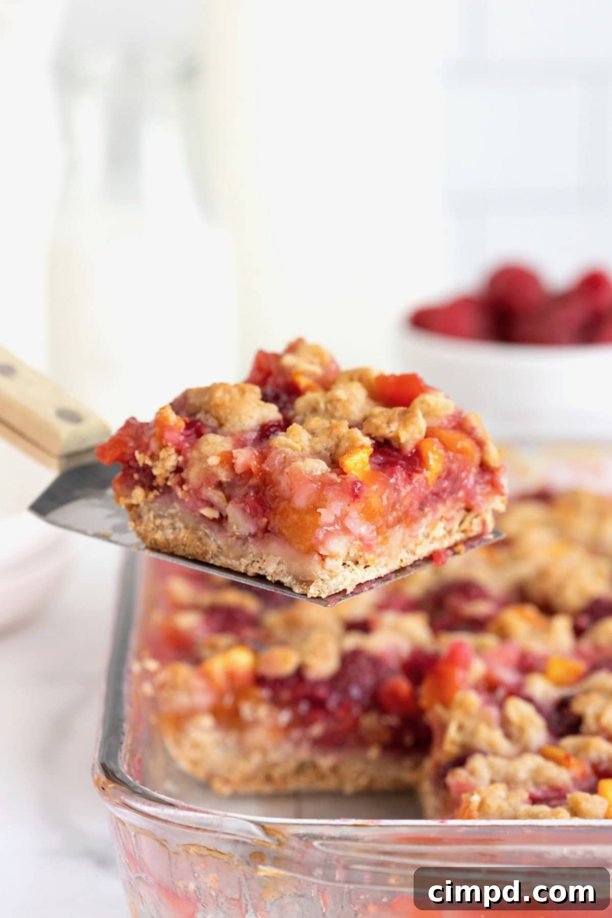 Rustic Peach Raspberry Crumbles 3 A peach raspberry crumb bar on a spatula being lifted from a baking dish.