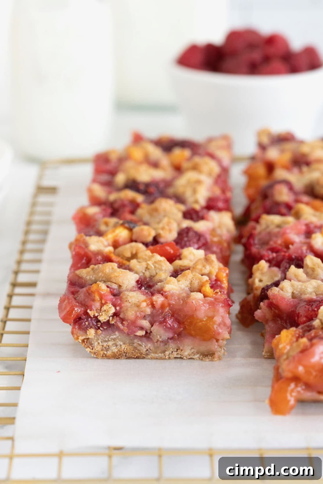 Rustic Peach Raspberry Crumbles 5 Peach raspberry crumb bars on a parchment lined gold-toned wire cooling rack.