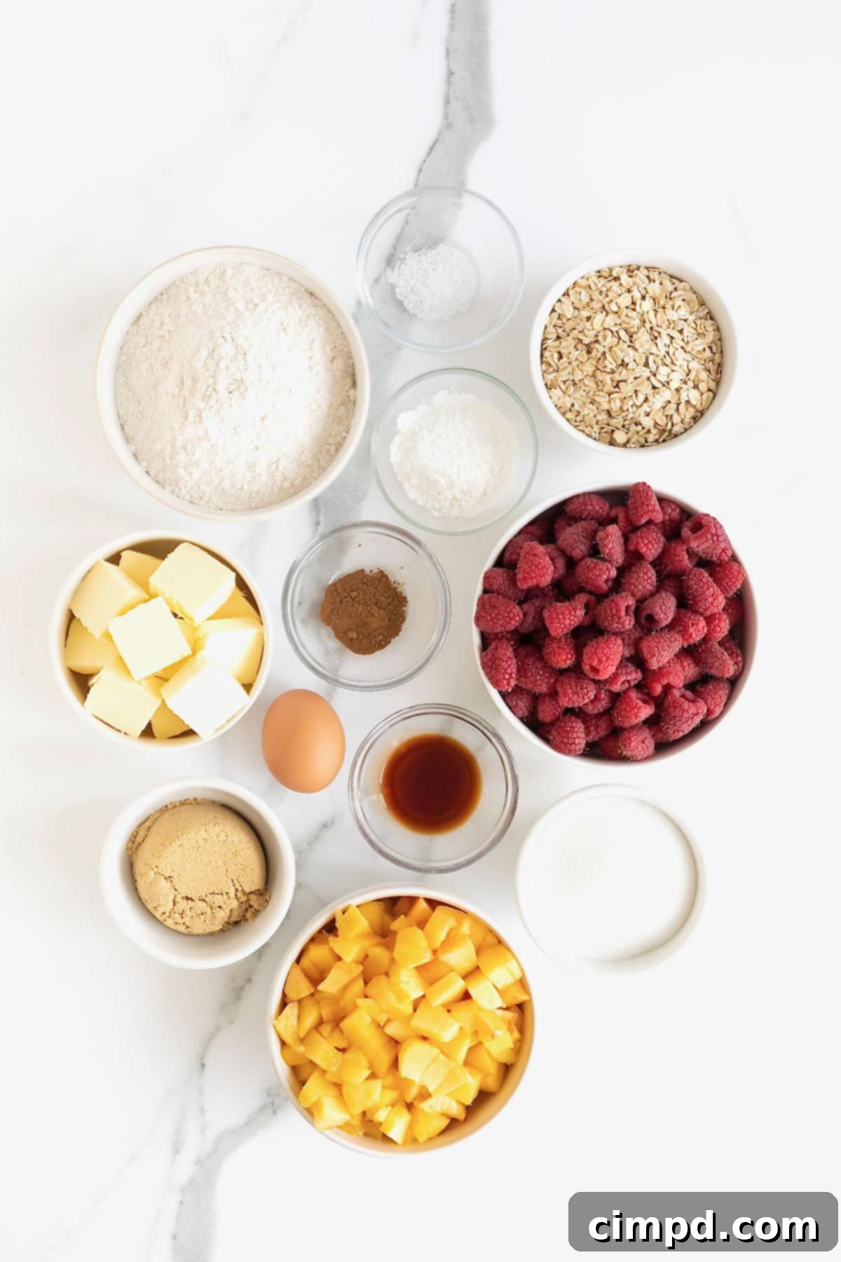 Golden Peach Raspberry Crumble Squares 6 An organized array of ingredients for peach raspberry crumb bars in small glass bowls, neatly arranged on a white marble countertop.