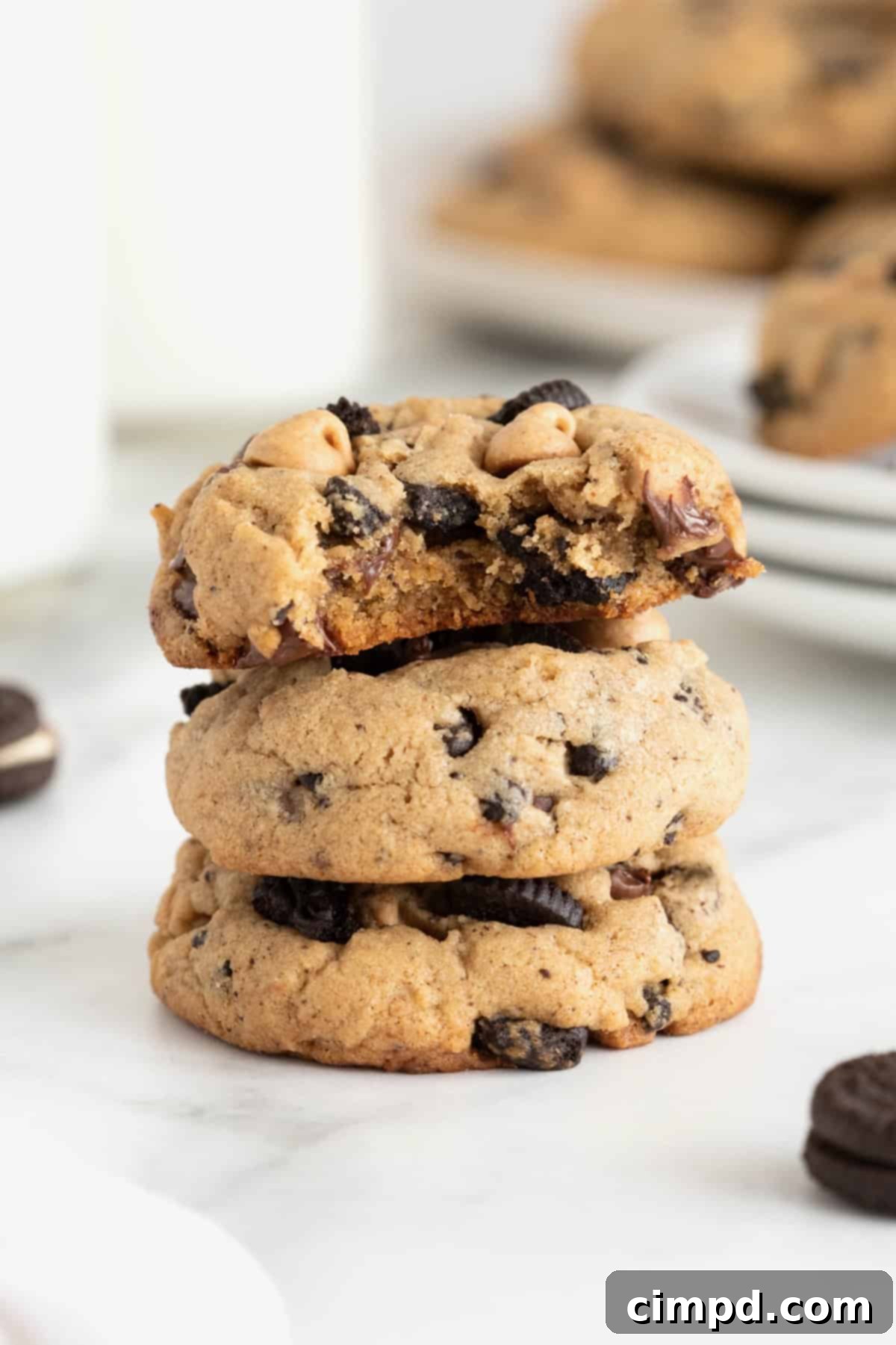 Three peanut butter Oreo cookies in a stack on a white marble counter. The top cookie has a bite out of it, revealing its chewy interior.