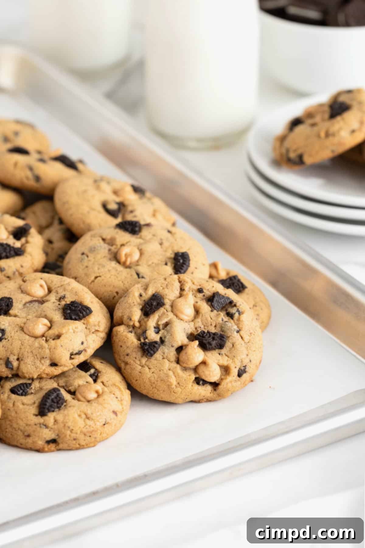 A row of eight freshly baked Peanut Butter Oreo cookies cooling on a parchment-lined cookie sheet, showcasing their golden-brown edges and inviting texture.