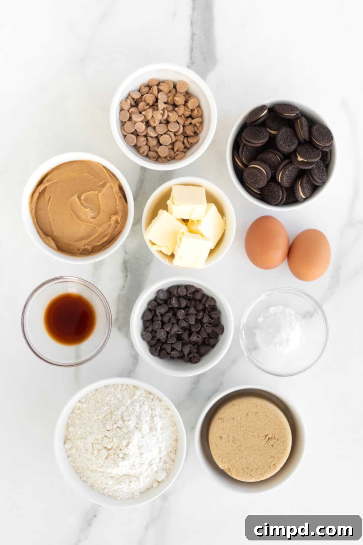 Ingredients to make peanut butter Oreo cookies in small white dishes on a white marble counter, neatly arranged.