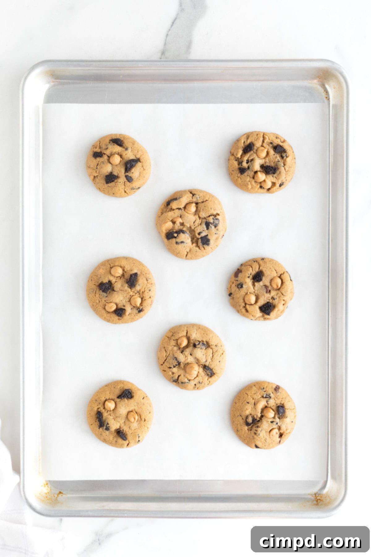 Eight peanut butter Oreo cookies on a parchment lined aluminum cookie sheet, cooling after baking.