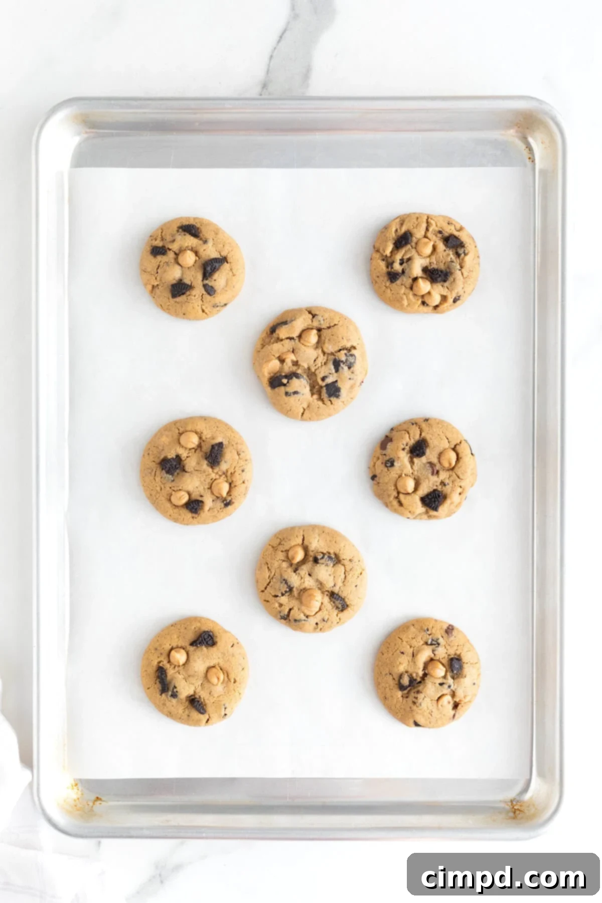 Eight perfectly baked Peanut Butter Oreo Cookies cooling on a parchment-lined aluminum cookie sheet, ready to be enjoyed.
