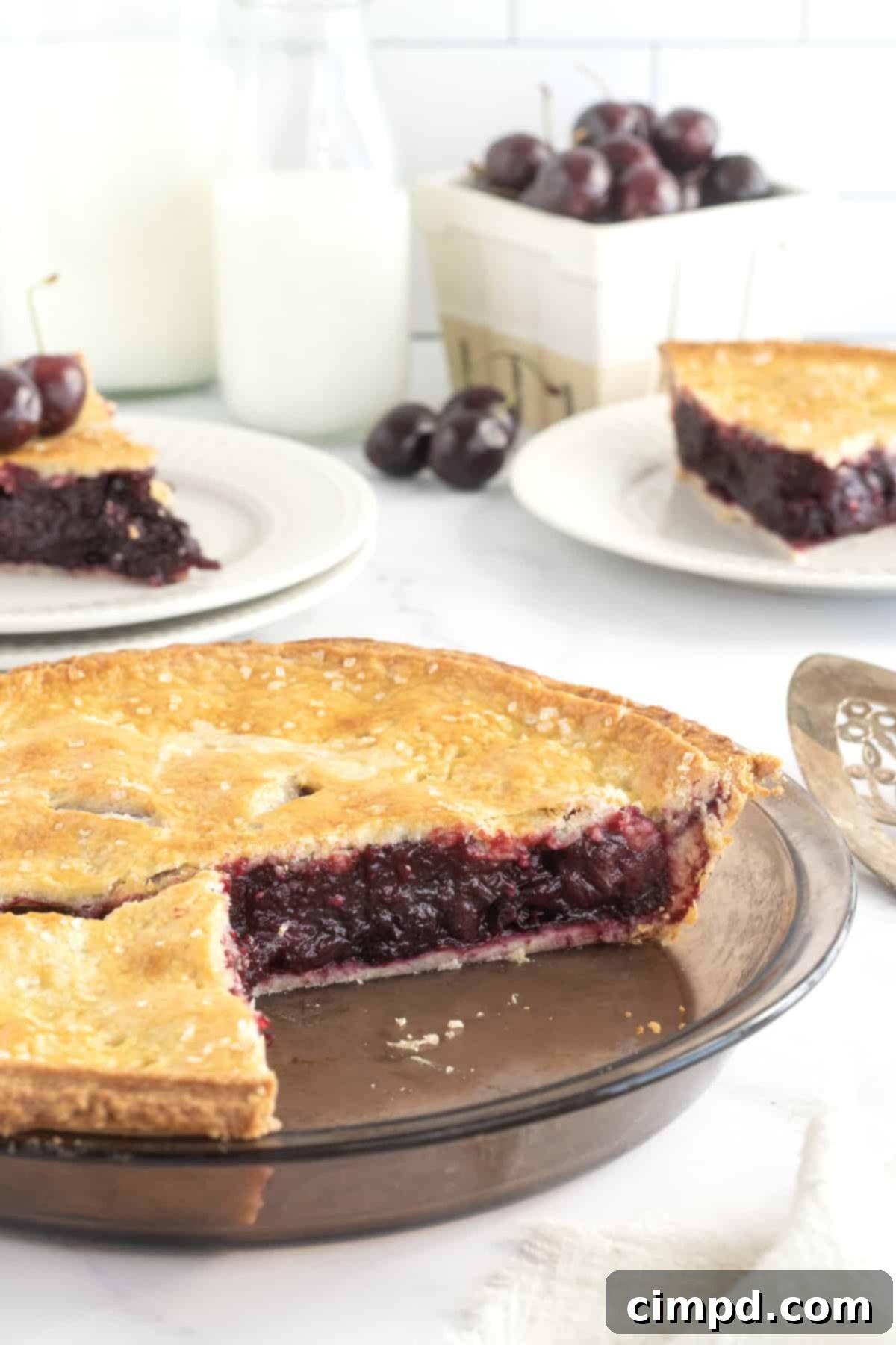 A cherry pie in a glass pie plate with a piece missing.