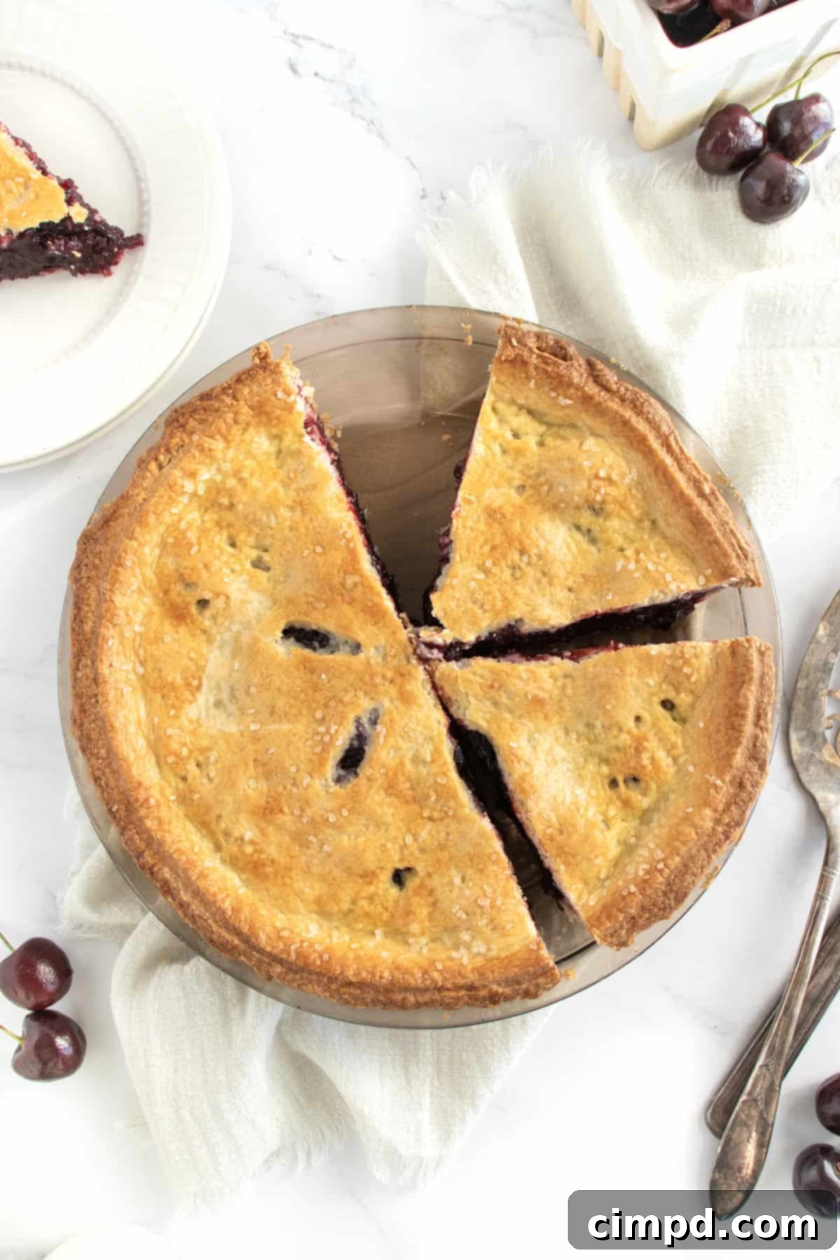A cherry pie in a glass pie plate cut in half with a piece missing.