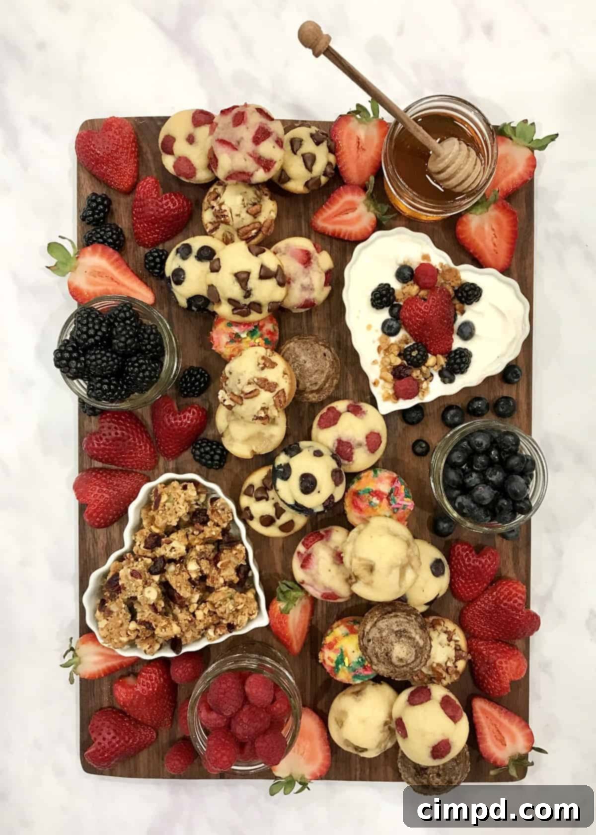 A stunning Mini Muffin Board adorned with various mini muffins, fresh berries, yogurt, granola, and honey, inviting guests to customize their breakfast experience. The board is beautifully arranged, perfect for a special occasion or a delightful family brunch.