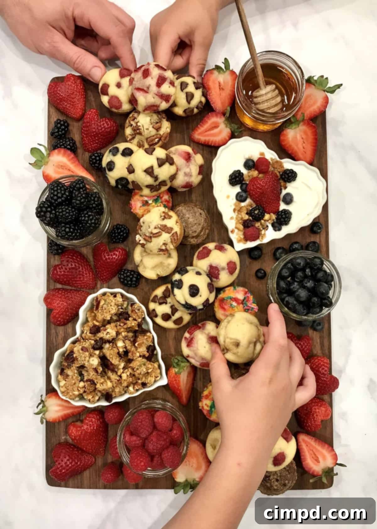 Close-up of a Mini Muffin Board showcasing an assortment of freshly baked mini muffins, including options with sprinkles, blueberries, and chocolate chips, surrounded by colorful fresh berries.