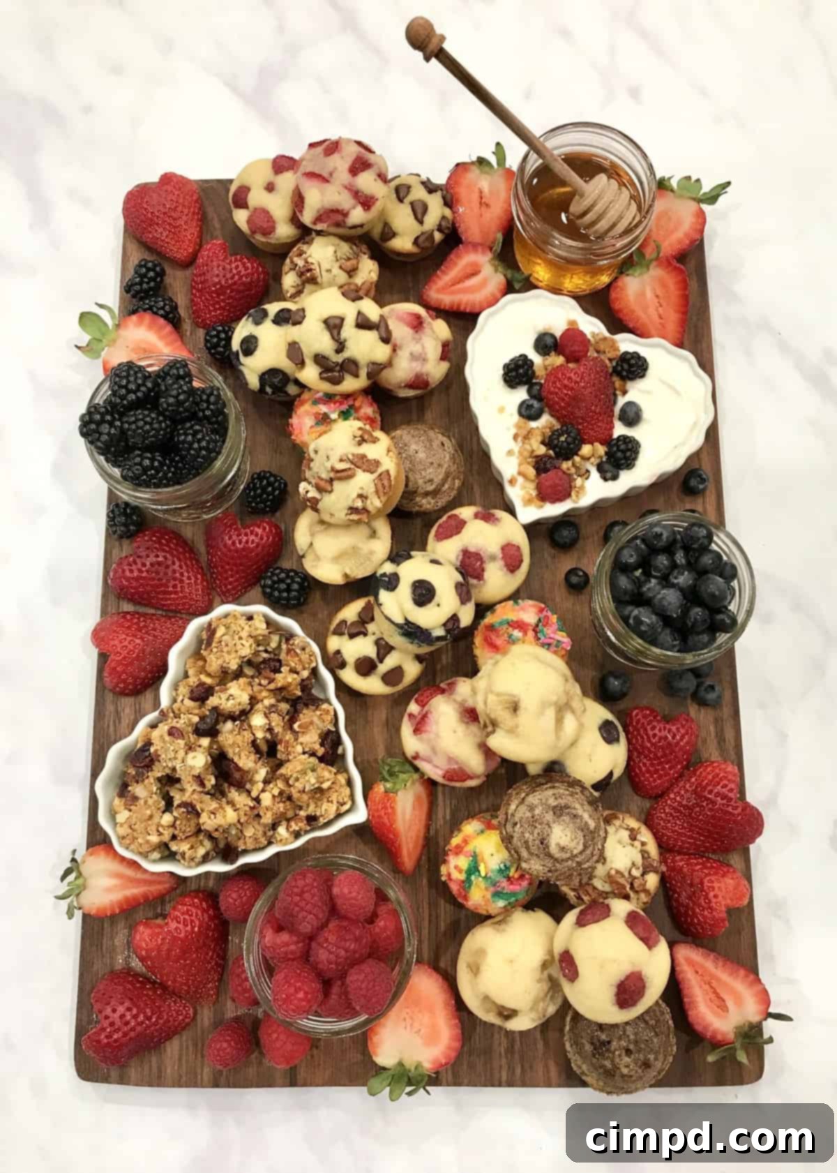 An overhead shot of a completed Mini Muffin Board, showcasing the beautiful arrangement of assorted muffins, various fresh berries, yogurt, granola, and honey, all ready to be enjoyed.
