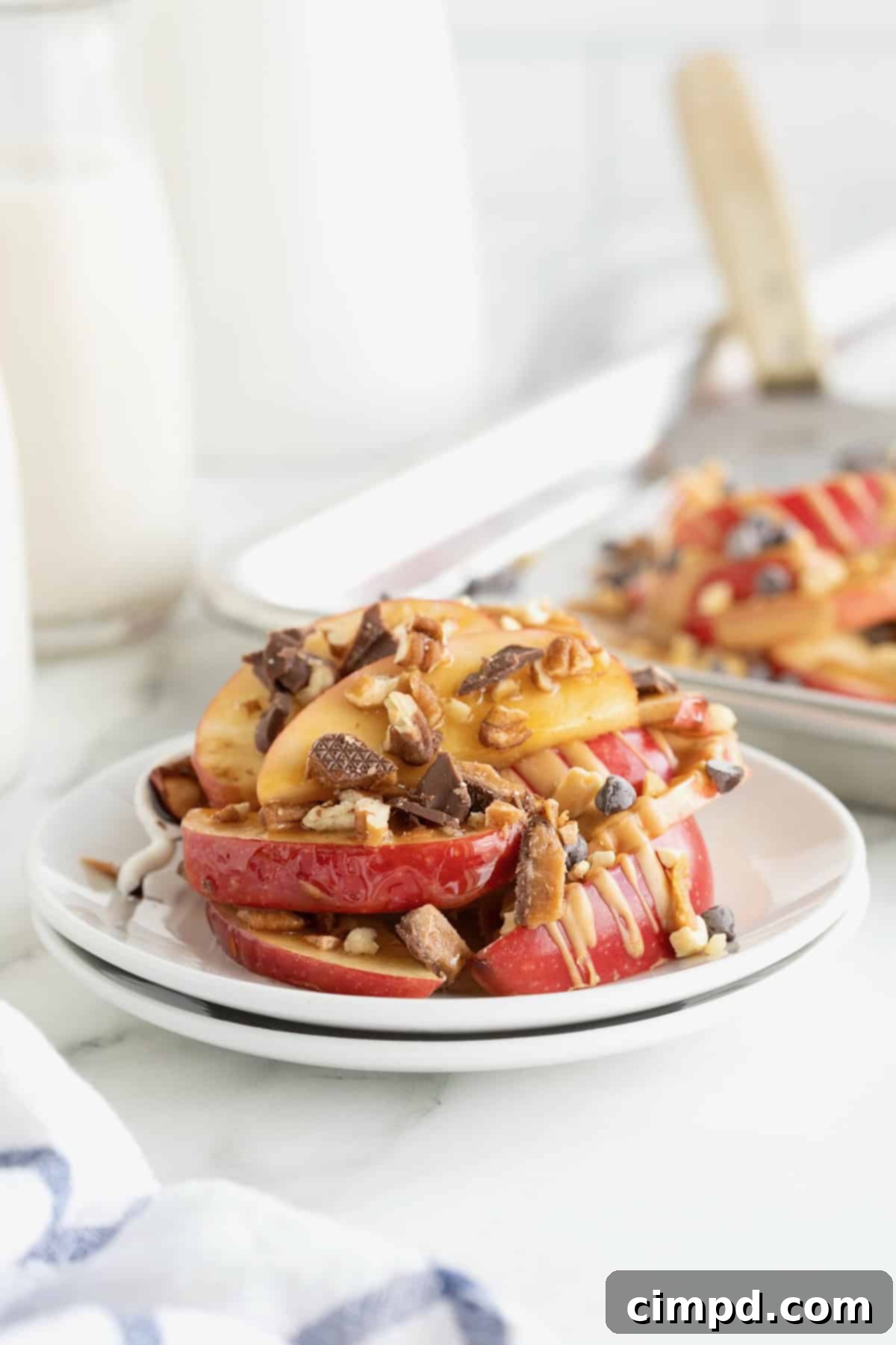 Loaded Apple Slices 4 A small white plate of apple nachos on a white marble counter. An aluminum sheet pan of apple nachos is in the background.