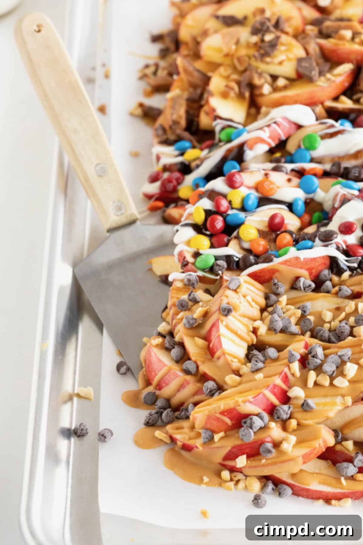 Loaded Apple Slices 8 A metal spatula with a wooden handle in a sheet pan of apple nachos.