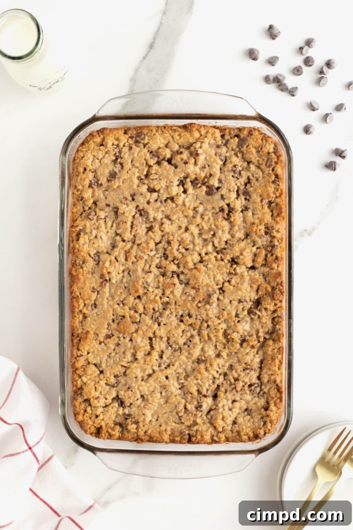 Homemade Chocolate Chip Granola Bars 9 A glass baking dish of granola bars on a white marble counter with chocolate chips scattered at the upper right corner.