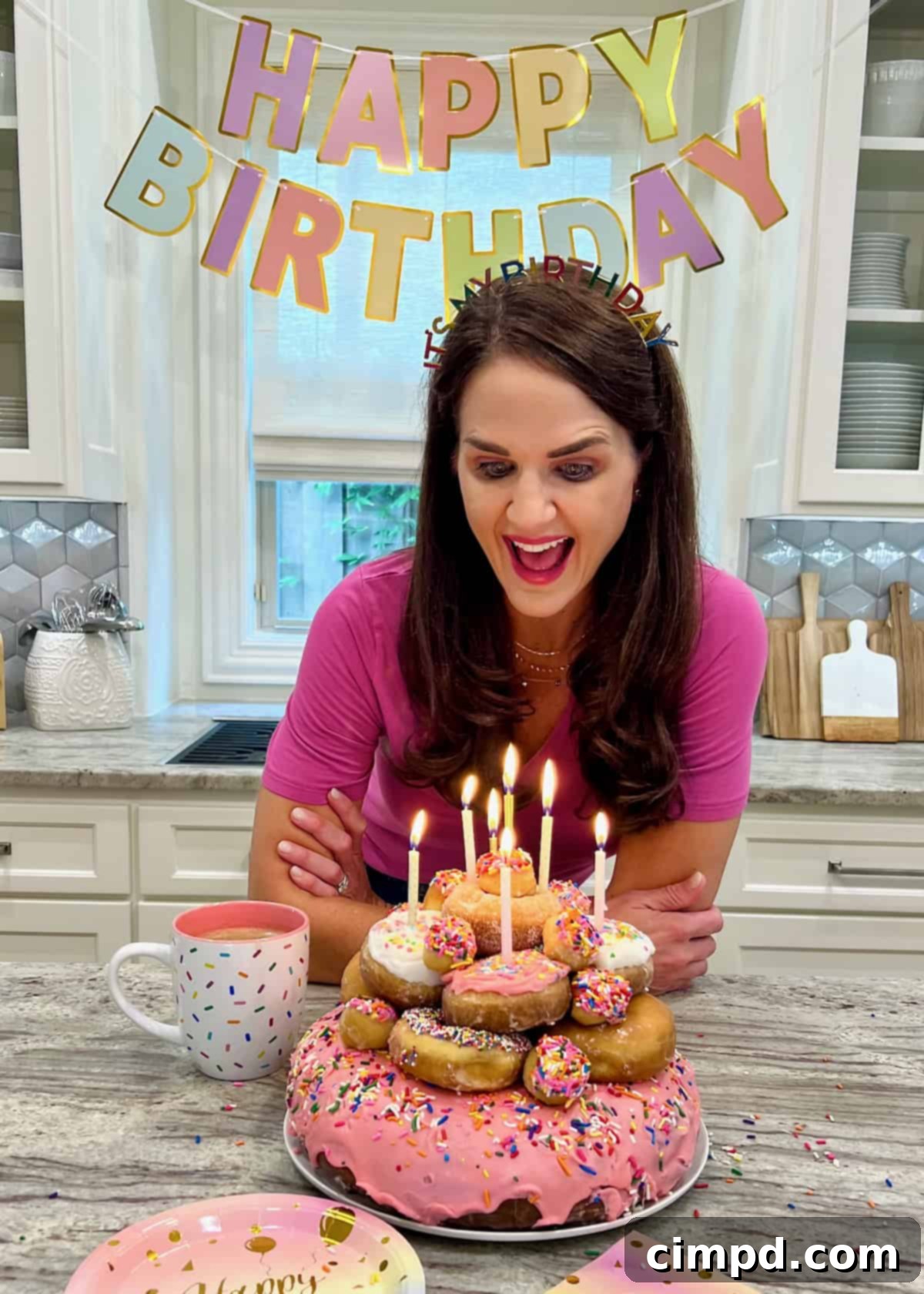 Maegan Brown joyfully leaning over to blow out seven candles on a beautifully arranged donut cake, surrounded by family.