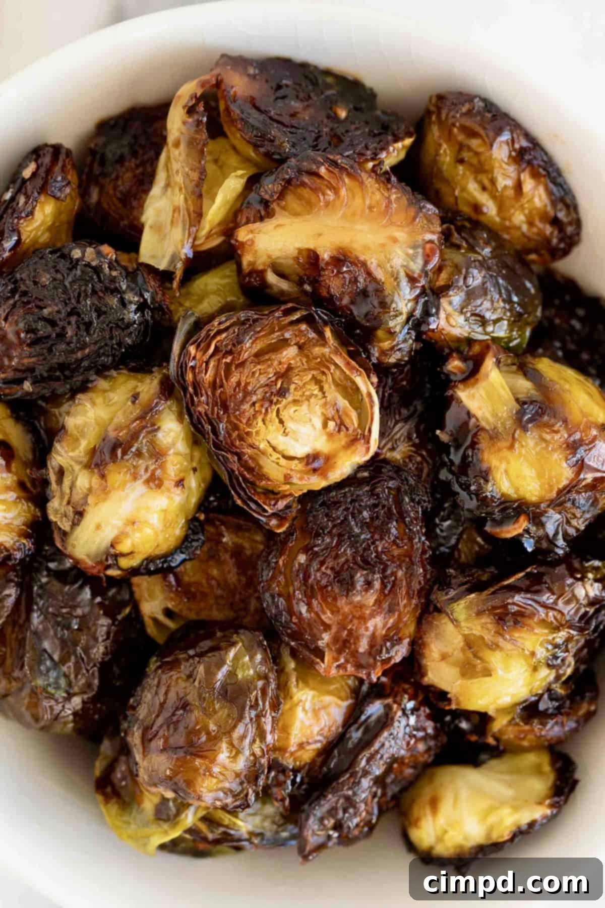 A close-up of charred Brussels sprouts halves covered in a rich, glistening sauce.