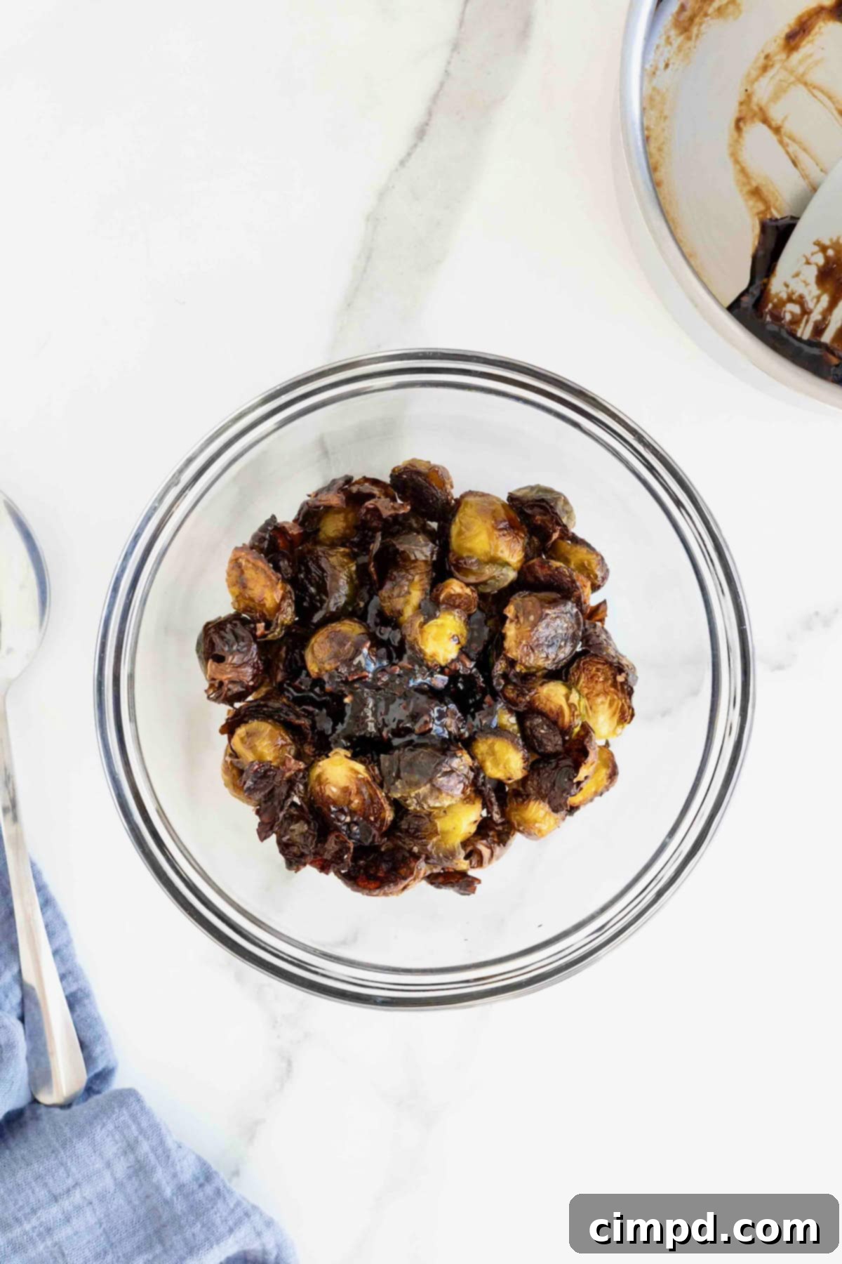 A glass mixing bowl of Brussels sprout halves tossed in sauce, showcasing their glazed finish.