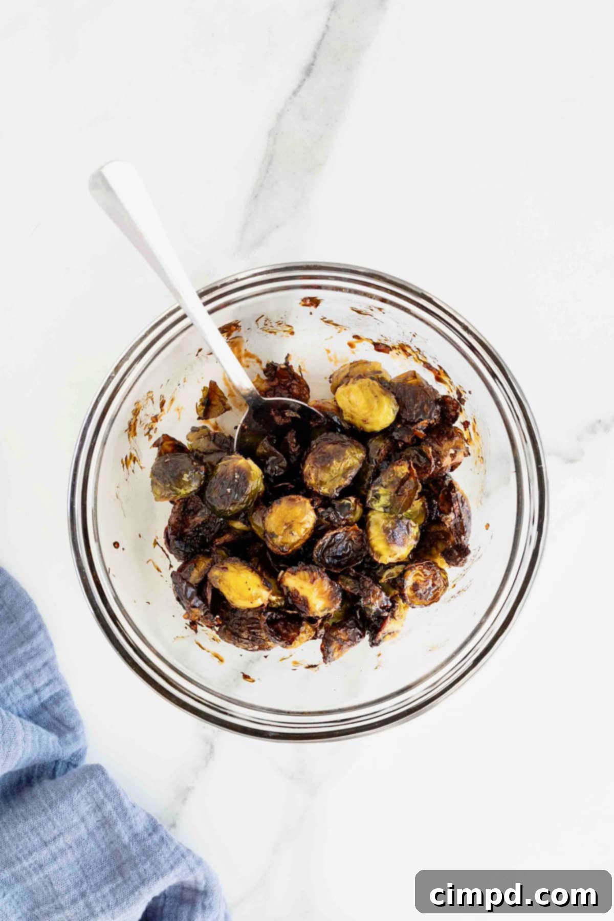 A glass mixing bowl of Brussels sprout halves tossed in sauce, ready for serving.