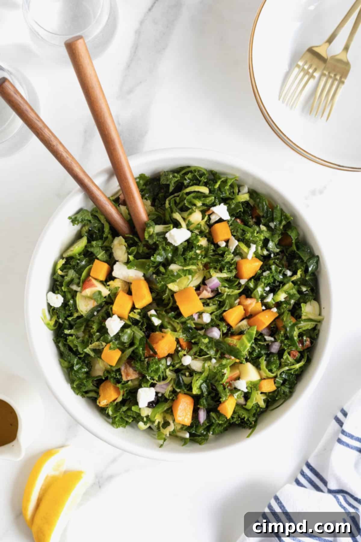 Vibrant Kale and Brussels Sprouts Salad 2 A large white serving bowl of kale salad with wooden salad spoons sticking out.