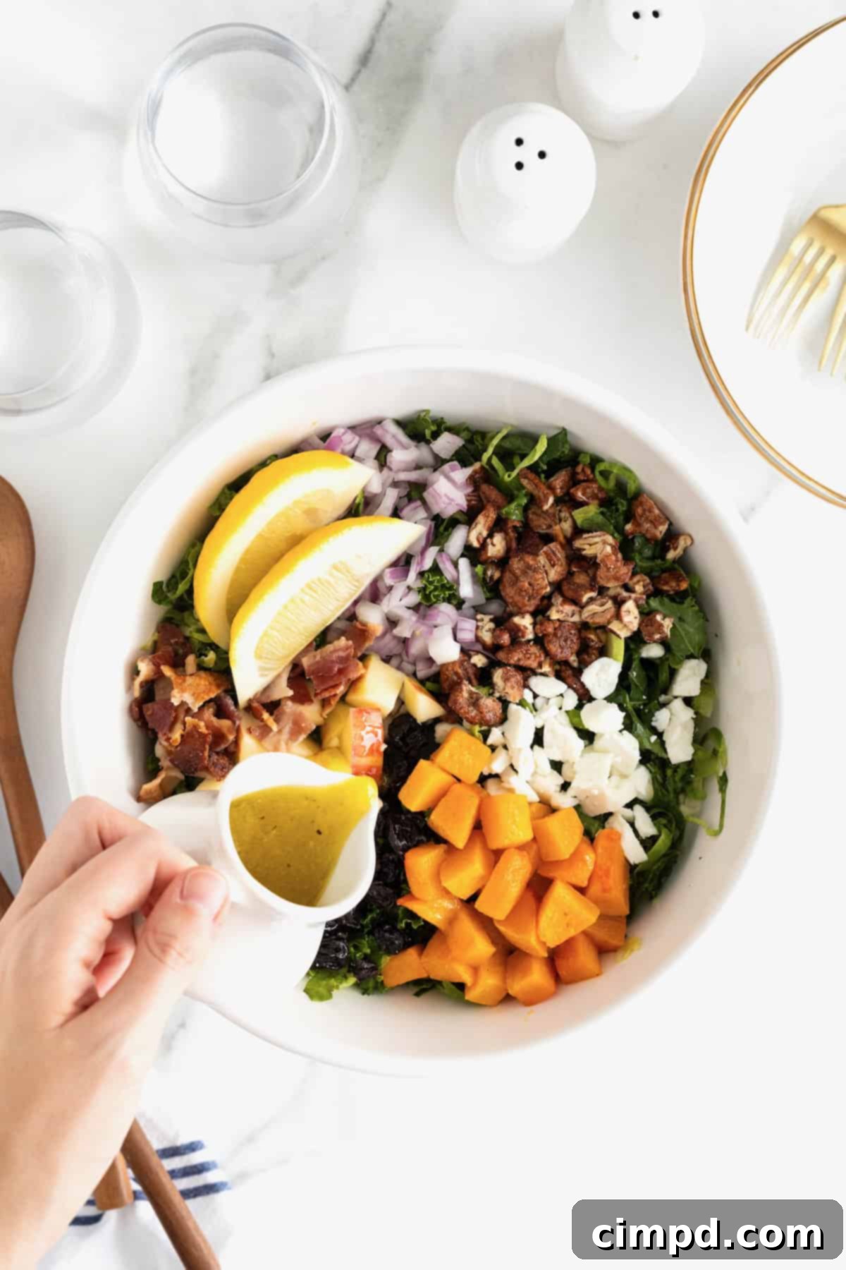Vibrant Kale and Brussels Sprouts Salad 9 Salad dressing being poured from a small white carafe over a colorful salad in a large white serving bowl.