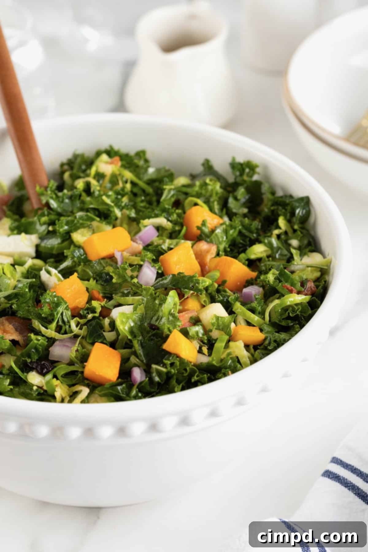 Vibrant Kale and Brussels Sprouts Salad 10 A large white serving bowl of kale salad with chunks of sweet potato.