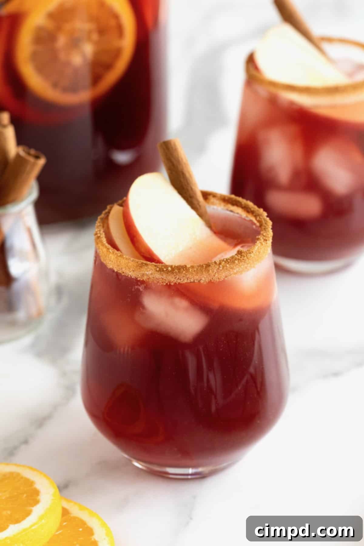 Spiced Apple Cider Sangria 2 A glass rimmed with cinnamon sugar filled with vibrant apple cider sangria, garnished with fresh apple slices and a cinnamon stick.