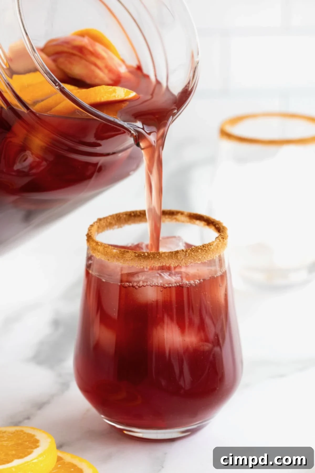 Spiced Apple Cider Sangria 3 Apple cider sangria being poured from a glass pitcher into a cinnamon sugar rimmed glass filled with ice and fruit.