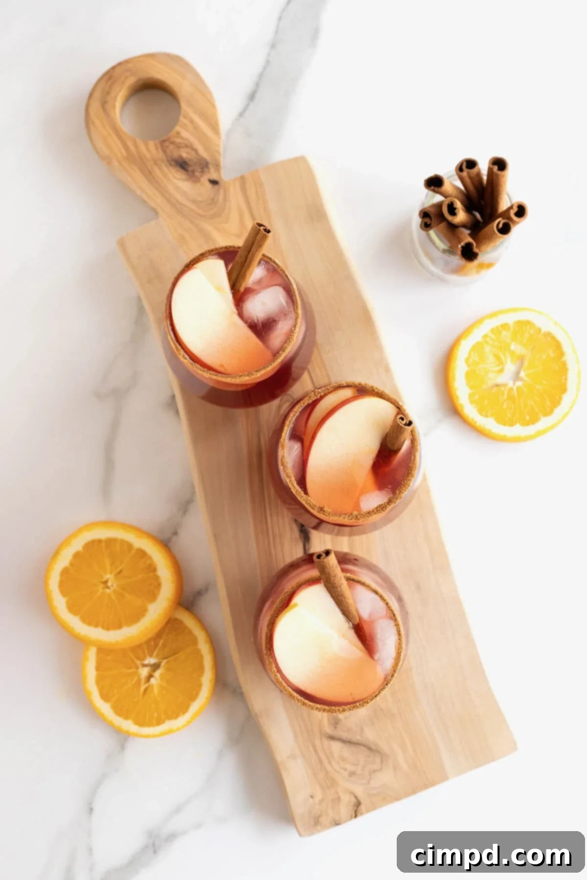 Spiced Apple Cider Sangria 4 Three elegant glasses of apple cider sangria arranged on a rustic wooden cutting board, ready for serving.