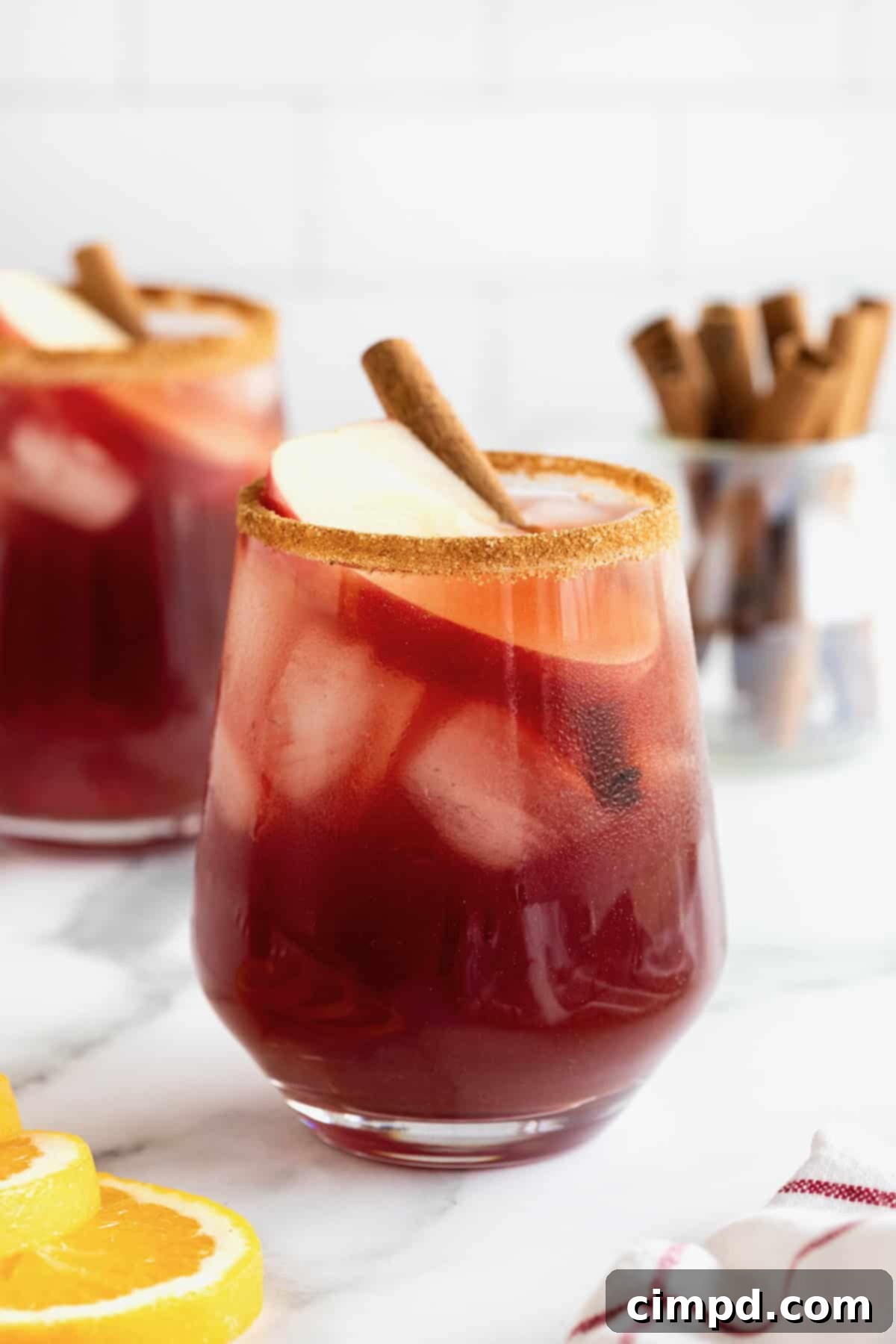 Spiced Apple Cider Sangria 5 Two glasses of sparkling apple cider sangria, expertly rimmed with cinnamon sugar, resting on a pristine white marble counter.