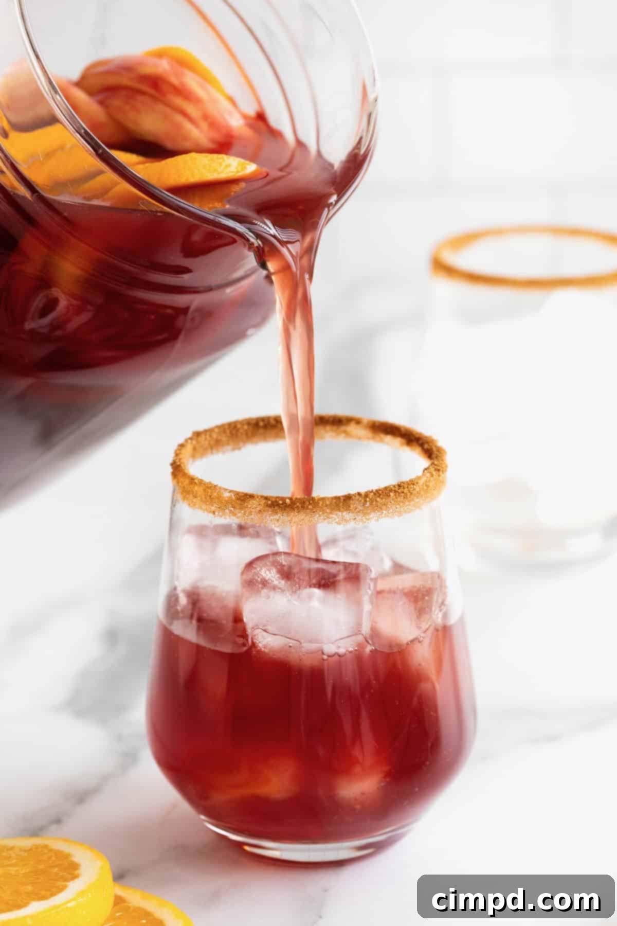 Spiced Apple Cider Sangria 9 Apple cider sangria being poured from a pitcher into a glass with a cinnamon sugar rim and ice.