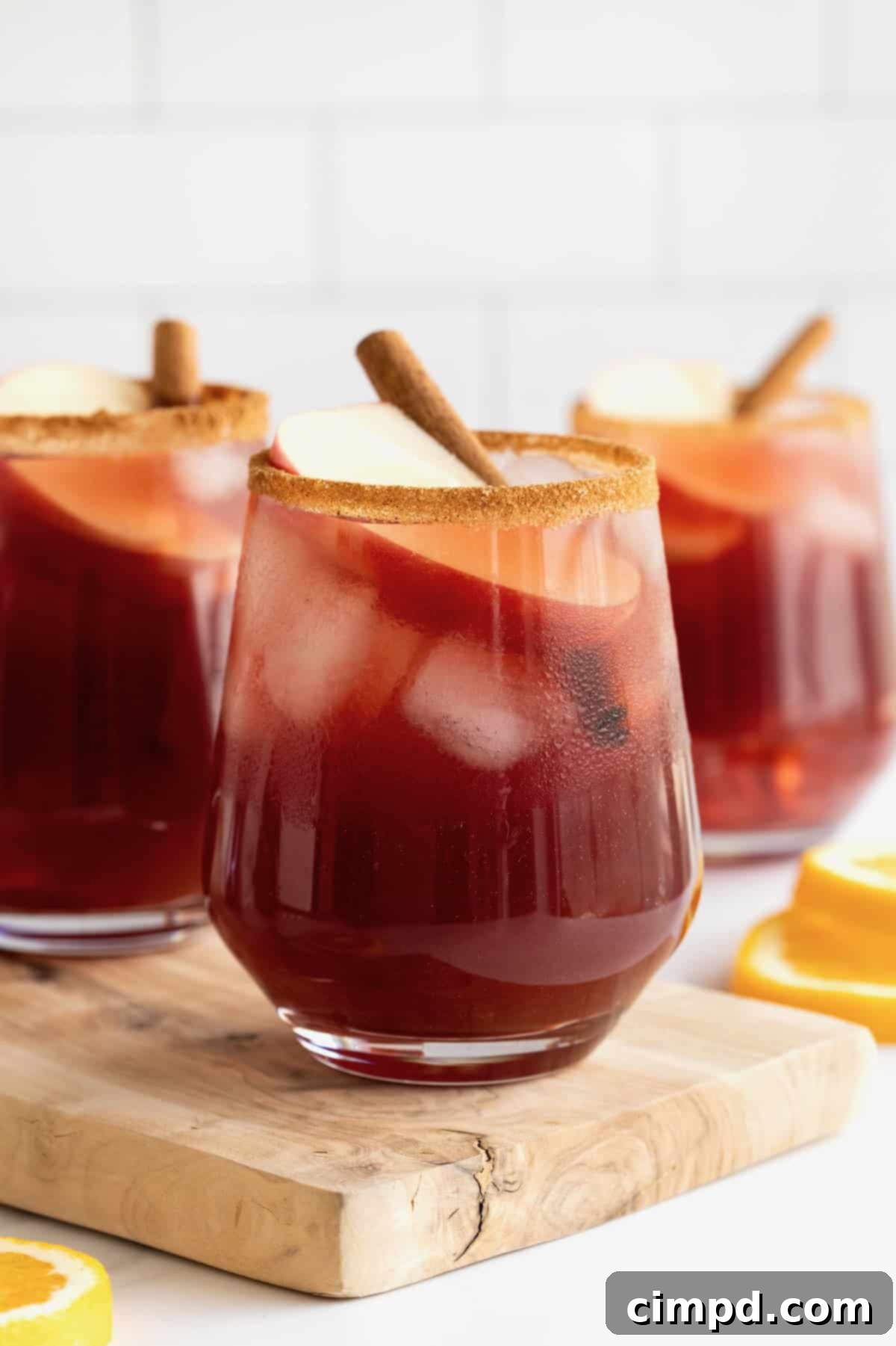 Spiced Apple Cider Sangria 10 Three glasses of apple cider sangria, beautifully garnished and ready to be enjoyed, displayed on a rustic wooden cutting board.
