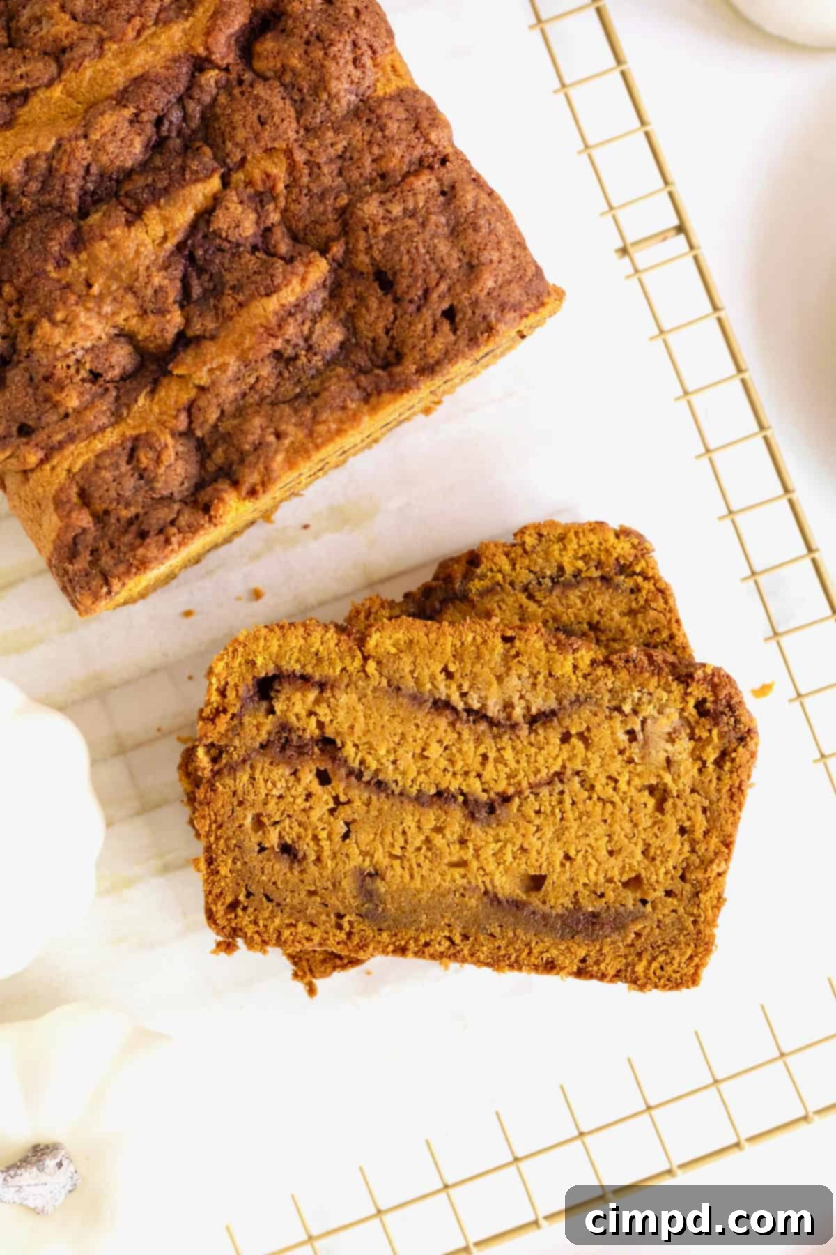 Sliced cinnamon swirled pumpkin bread on a parchment lined, gold tone cooling rack, showcasing the beautiful cinnamon swirl.