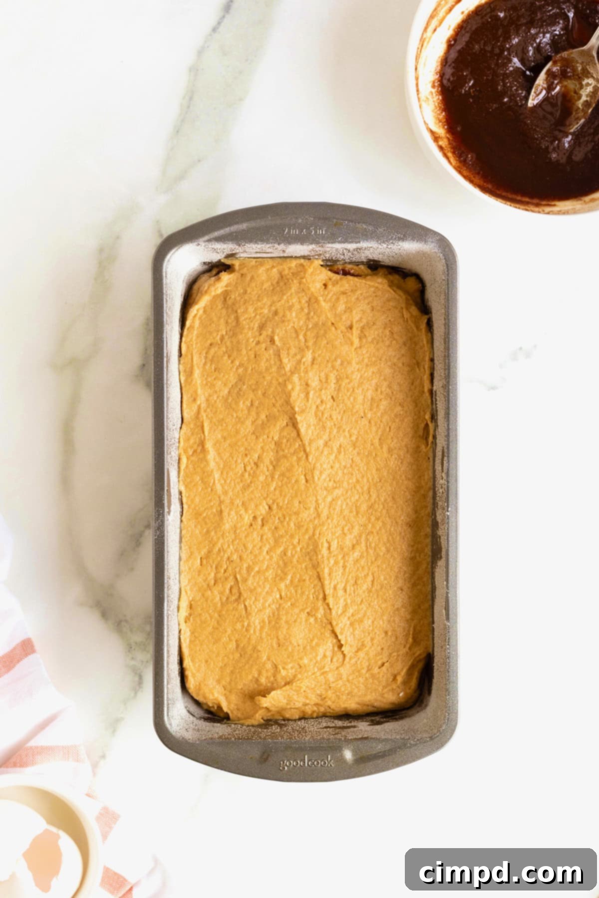 Pumpkin bread batter meticulously layered in an aluminum loaf pan, ready for the final cinnamon swirl.