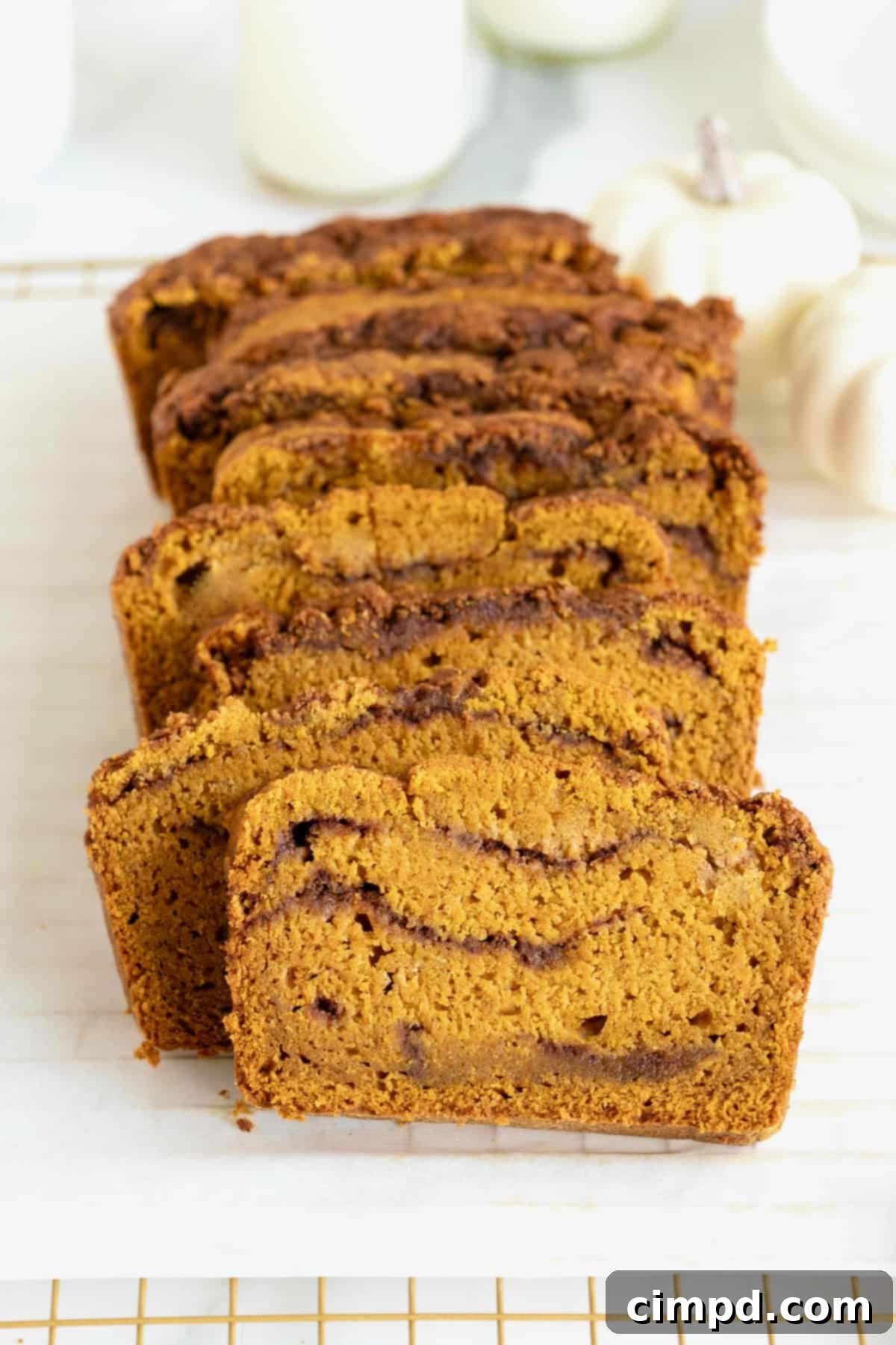 Beautifully sliced cinnamon swirled pumpkin bread arranged on a parchment lined, gold tone cooling rack, ready to be enjoyed or stored.