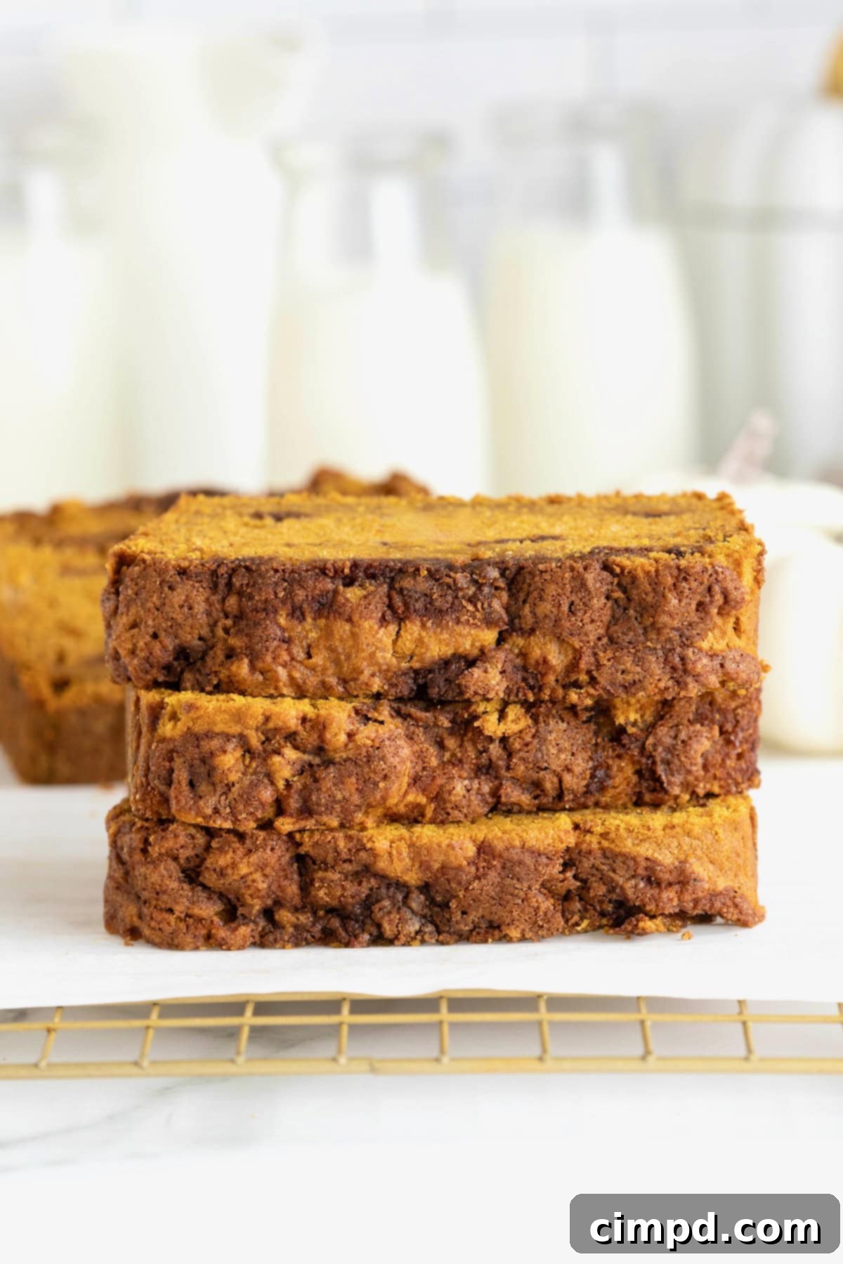 Three decadent slices of cinnamon swirled pumpkin bread arranged artfully on a parchment lined cooling rack.