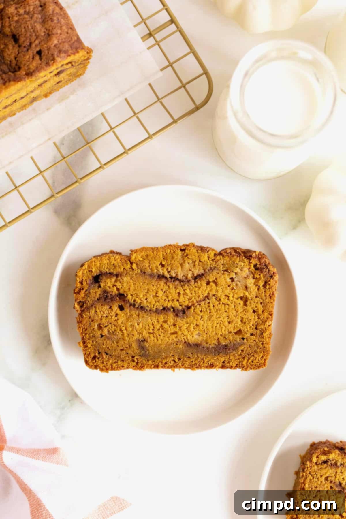 A single slice of cinnamon swirled pumpkin bread resting on a small, elegant white-rimmed plate.