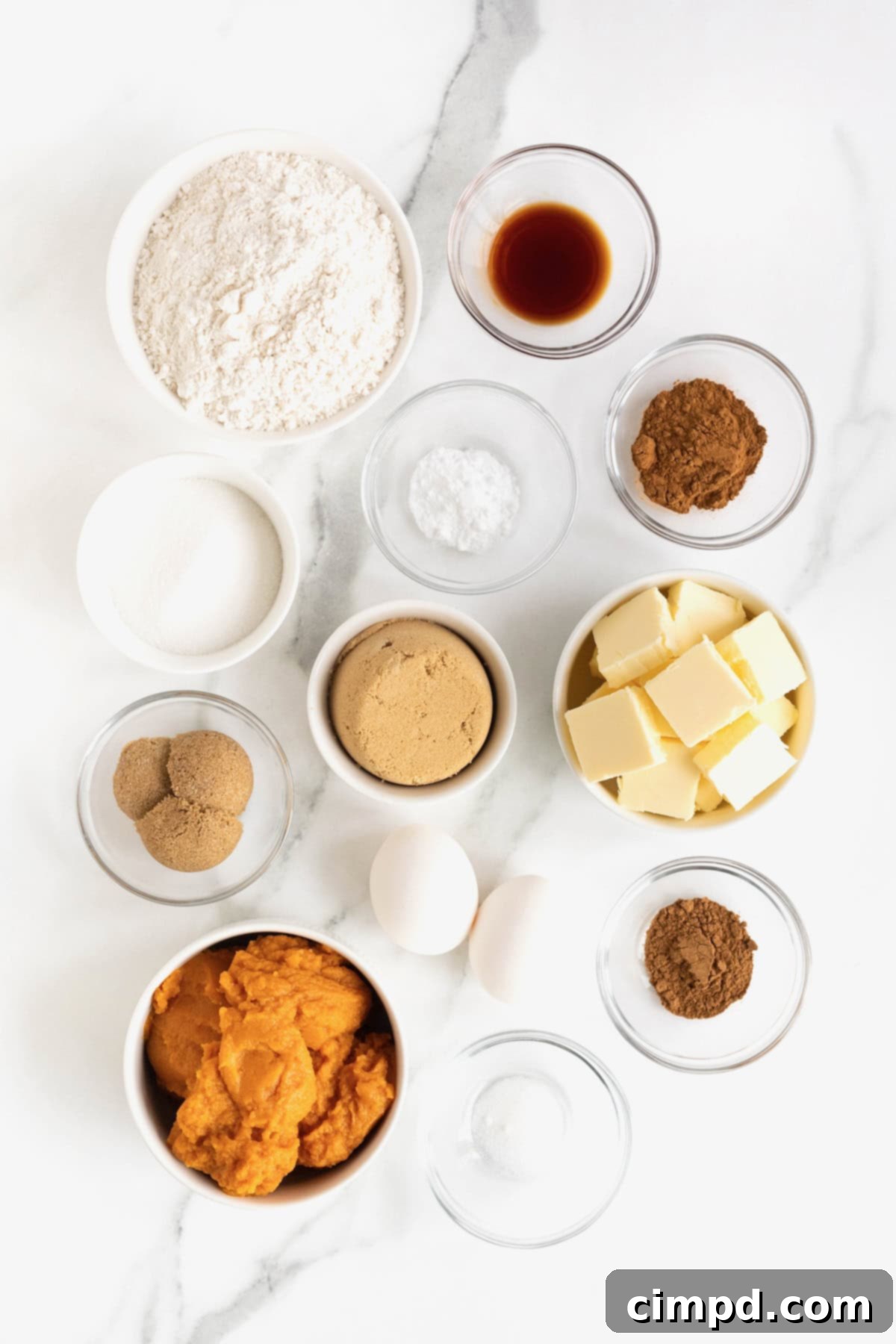 A beautiful display of ingredients for cinnamon swirled pumpkin bread, neatly arranged in small glass dishes on a pristine white marble counter.