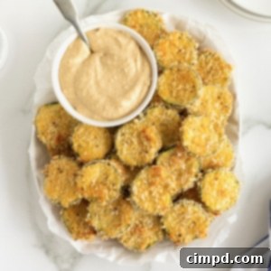 Crispy Zucchini Snacks 11 An oblong white serving platter of zucchini chips surrounding a bowl of hummus with a metal spoon in it.